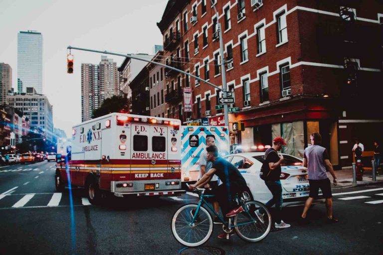 people crossing city street in front of ambulance